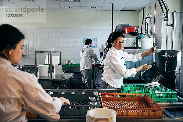 Female chef washing dishes in commercial kitchen