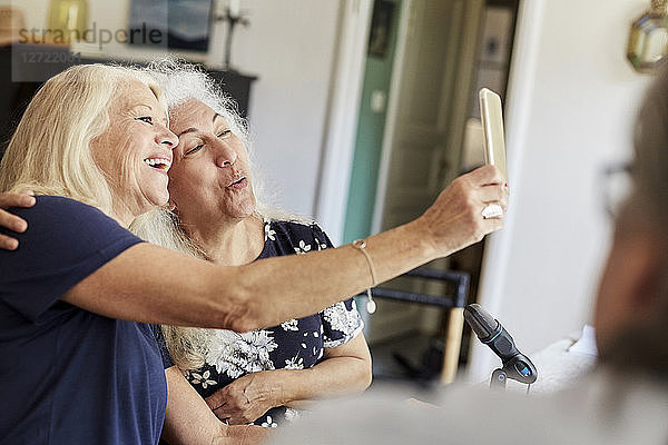 Happy senior friends taking selfie on mobile phone while vlogging at home