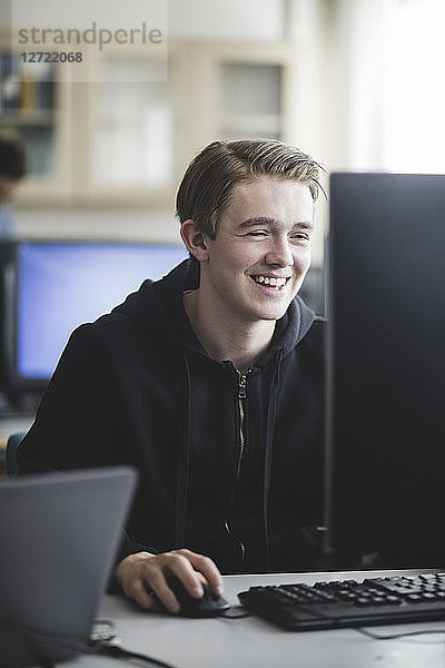 Smiling teenage boy using computer in classroom at high school