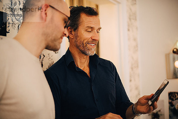 Mature man showing mobile phone to friend during party at home