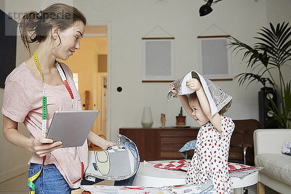 Fashion designer with digital tablet looking at playful daughter holding textile