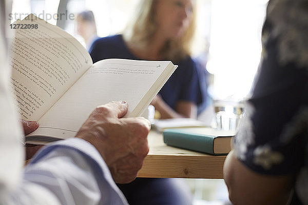 Cropped image of senior man reading book while sitting with friends at restaurant