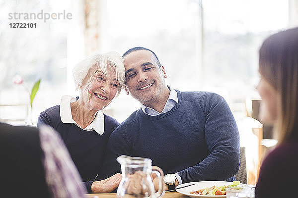 Smiling senior woman sitting with son while having lunch at table in nursing home
