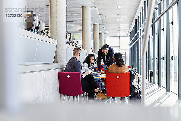 Young man discussing with friends while studying at cafeteria in university