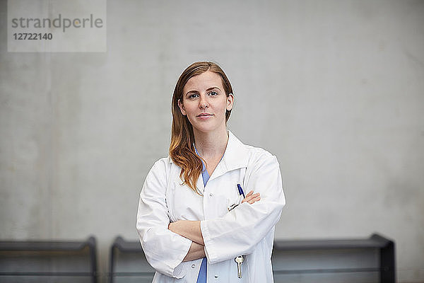 Portrait of confident female doctor standing with arms crossed against wall at hospital