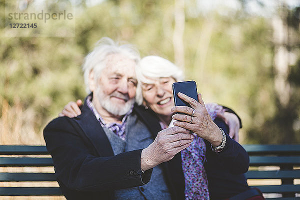 Smiling senior couple taking selfie while sitting on bench