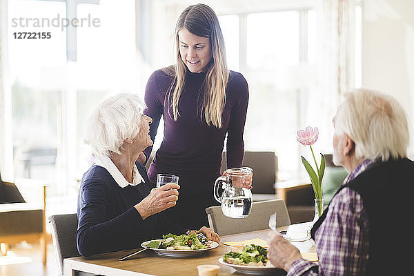 Young woman talking with grandmother while grandfather having meal at table in nursing home