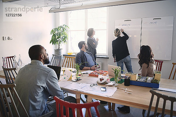 Female engineer explaining colleagues over whiteboard during meeting in office