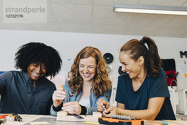 Smiling multi-ethnic technicians working on wood at workbench in creative office