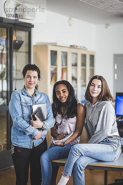 Portrait of confident female teacher standing by high school students in computer lab