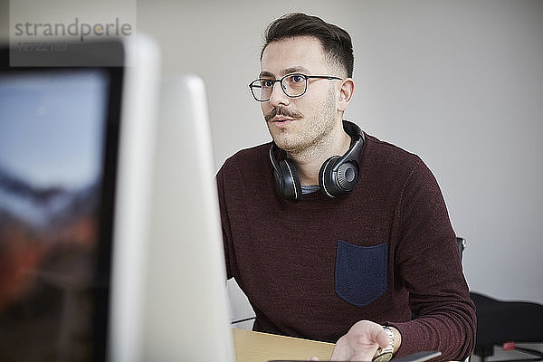 Businessman wearing headphones while using laptop at desk in office