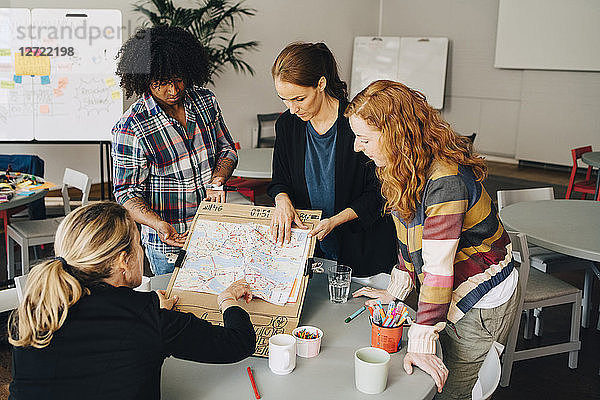 Multi-ethnic students showing map on placard to female manager at table in creative office