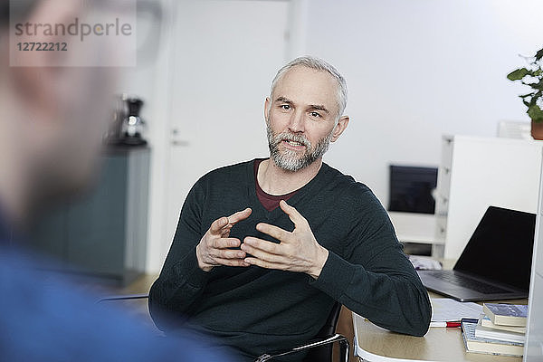 Mature businessman gesturing while discussing with coworker at desk in office