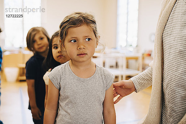 Midsection of teacher standing with students in classroom at child care