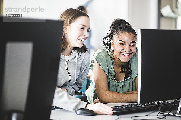 Cheerful multi-ethnic teenage girls discussing at desk in computer lab at high school