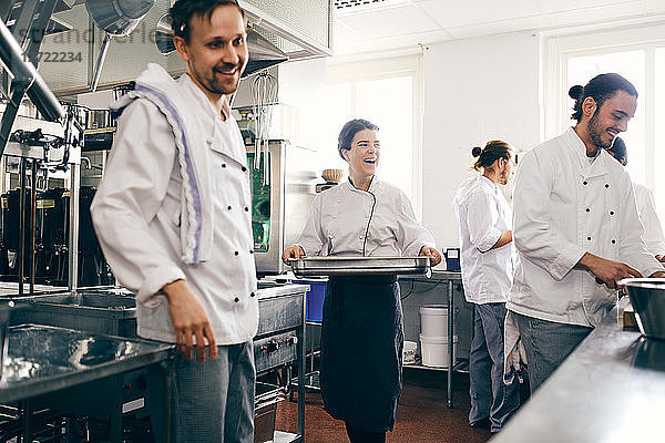 Smiling female chef with colleagues working in commercial kitchen