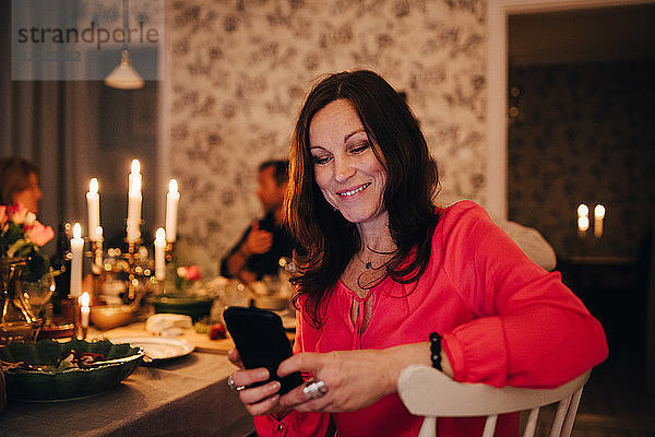 Smiling woman using mobile phone while sitting with friends in dinner party