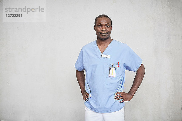 Portrait of confident mid adult male nurse standing with hands on hips in corridor at hospital