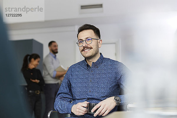 Smiling businessman holding coffee cup while sitting at office