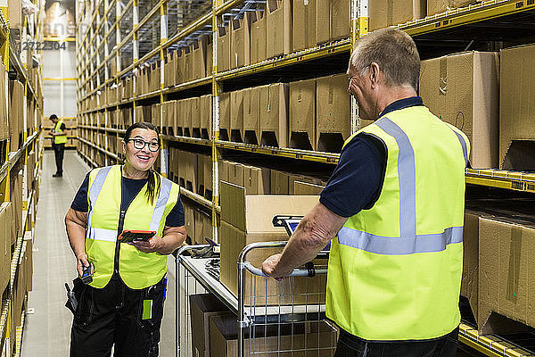 Smiling coworkers discussing while standing on aisle amidst racks at distribution warehouse