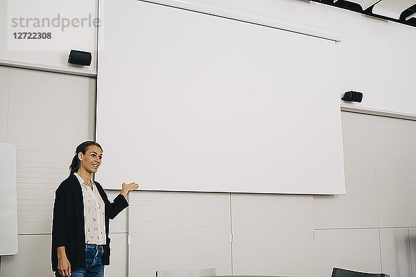 Smiling businesswoman giving presentation over blank projection screen at creative office