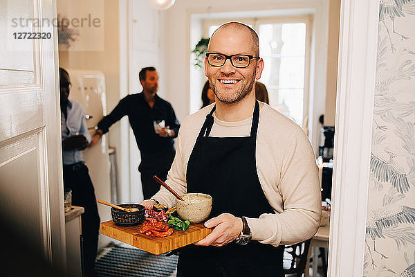 Portrait of man holding food in serving tray while standing at doorway