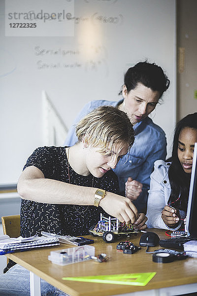 Mature female teacher looking at students preparing toy car on desk in classroom