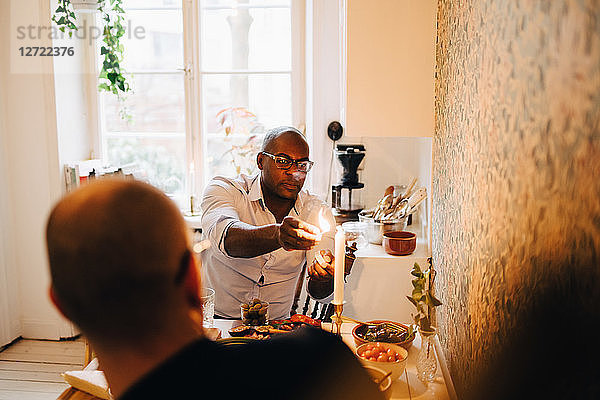 Man lighting candle while sitting with friend during dinner party at table