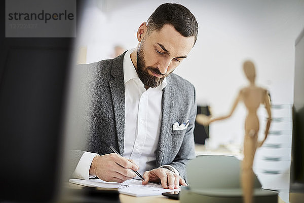 Mid adult businessman writing in note pad at desk in office