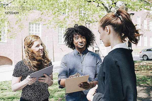 Confident businesswoman discussing with multi-ethnic colleagues while standing outdoors