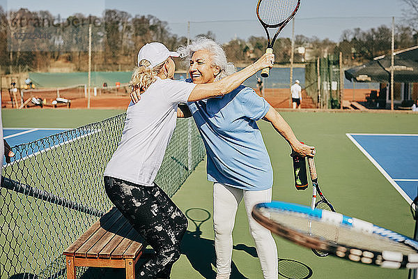 Happy female senior friends greeting at tennis court during summer