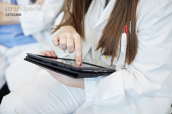Midsection of young female doctor using digital tablet while sitting in corridor at hospital