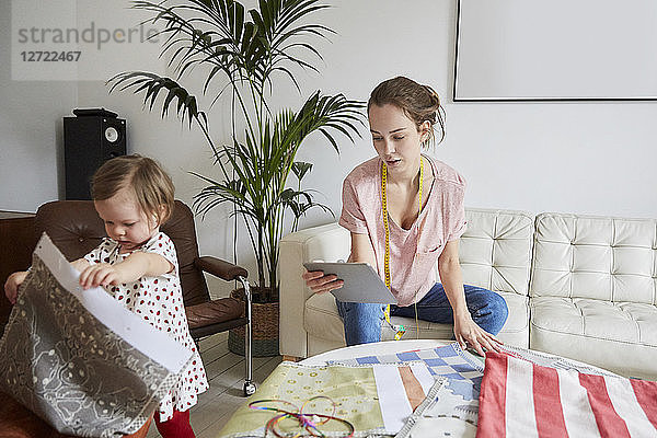 Fashion designer with digital tablet examining textile while daughter playing at home