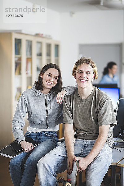 Portrait of smiling high school students sitting on desk in computer lab