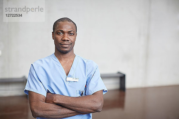 Portrait of confident mid adult male nurse standing with arms crossed in corridor at hospital