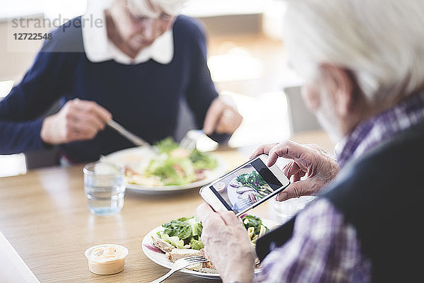 Senior man photographing food using smart phone while having lunch with woman at table