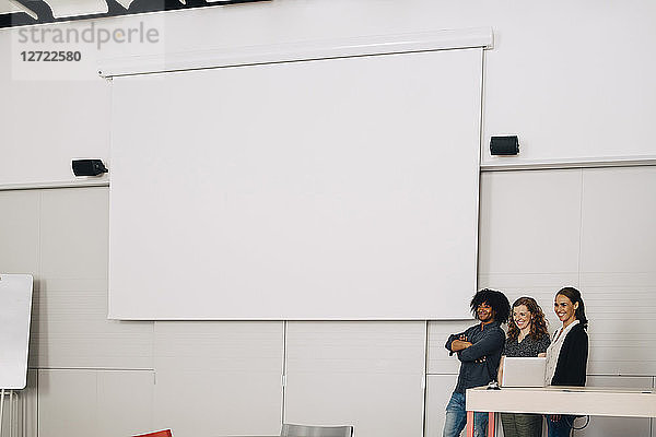 Smiling multi-ethnic technicians standing by blank projection screen at creative office