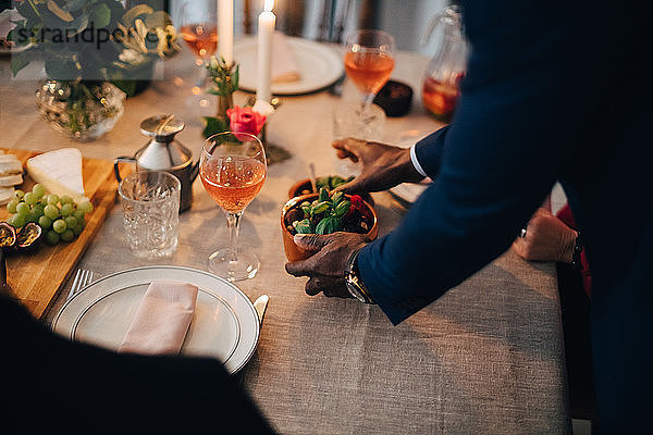 Midsection of man serving food to friend at dinning table in dinner party