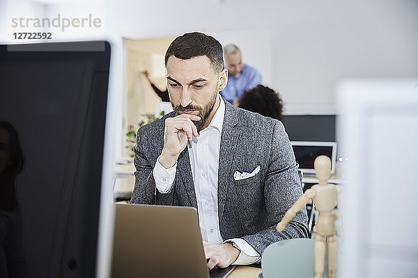 Serious businessman using laptop at desk in office