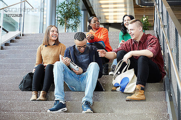 Low angle view of happy male and female friends talking while sitting on steps at university