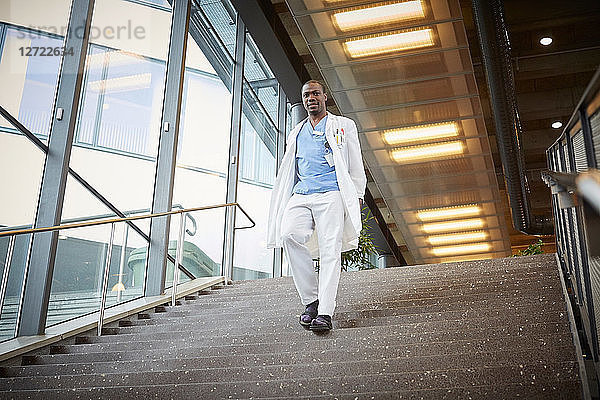 Low angle view of confident male doctor moving down on staircase at hospital