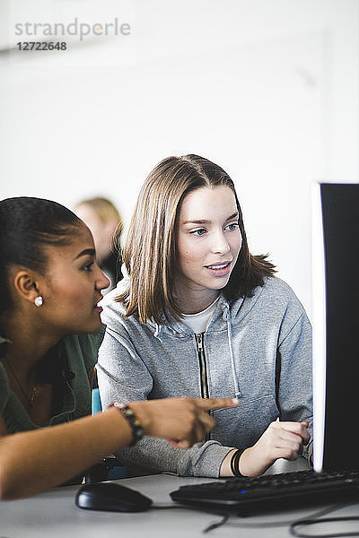 Multi-ethnic teenage girls discussing over computer monitor at desk in classroom