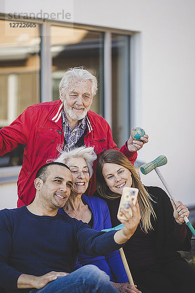 Cheerful multi-generation family taking selfie outside nursing home