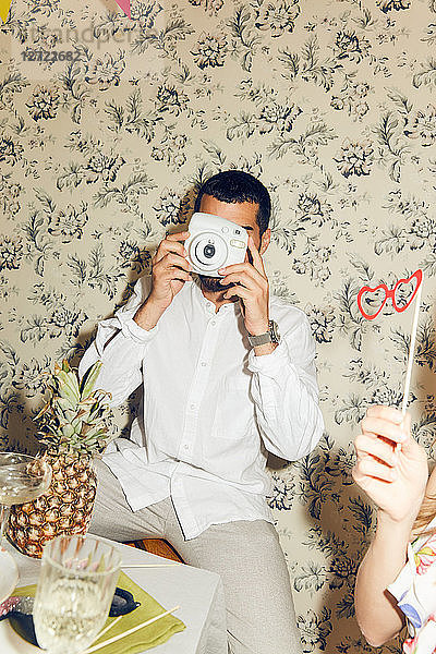 Young man photographing while sitting during dinner party at home