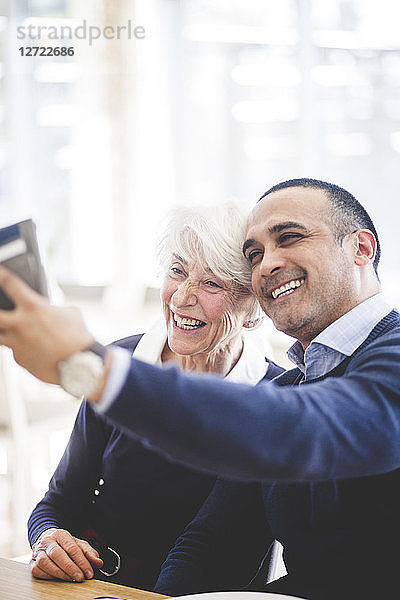 Cheerful mature man taking selfie with mother while sitting at table in nursing home