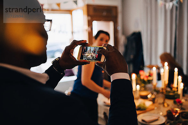 Man photographing friends through smart phone at dinner party