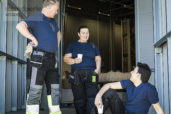 Smiling multi-ethnic workers discussing during coffee break at entrance of distribution warehouse