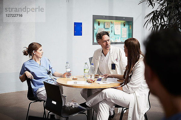 Confident mature doctor discussing with female coworkers while sitting at table in hospital cafeteria