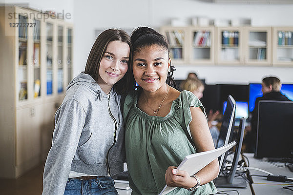 Portrait of happy female teenage friends standing in computer lab at high school