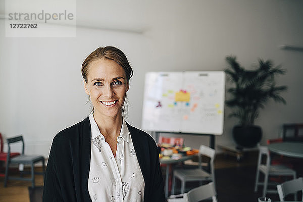 Portrait of smiling mid adult businesswoman standing at creative office